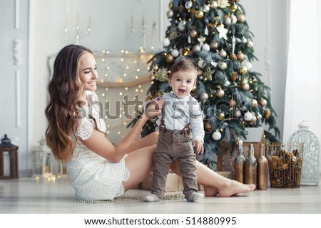 Portrait of happy mother and adorable baby celebrate Christmas. New Year\'s holidays. Toddler with mom in the festively decorated room with Christmas tree and decorations.