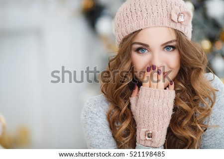 beautiful woman in warm clothing on christmas tree background. Very beautiful girl with blue eyes in a white hat costs about silver Christmas tree and smiling, close up