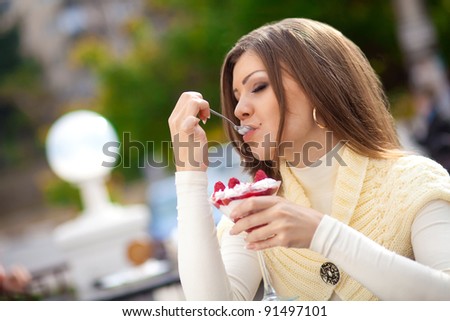 Portrait of cute young woman sitting in a cafe outdoor tasting a dessert