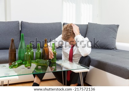 Depressed businessman drunk at home with empty bottles on table