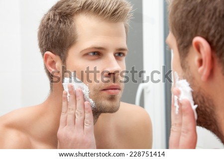 Handsome unshaven man looking into the mirror in bathroom