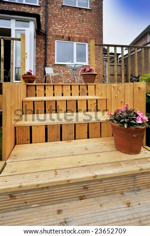 house with wooden decking and patio leading to garden