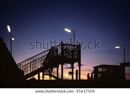 A station on a railway line in the countryside - two people in silhouette against a sunset standing on the platform