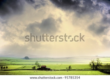 farm in the middle of farmland and fields - a shaft of light after a passing storm near shap, cumbria, england uk