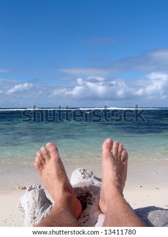 Two feet resting on a log on the beach