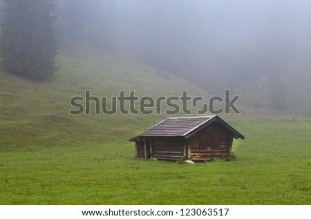 old wooden hut on alpine meadows covered with fog