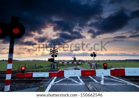 closed rail crossing with red signals at sunrise and windmill