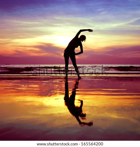 Silhouette of young woman, yoga stretching exercises on the beach at sunset