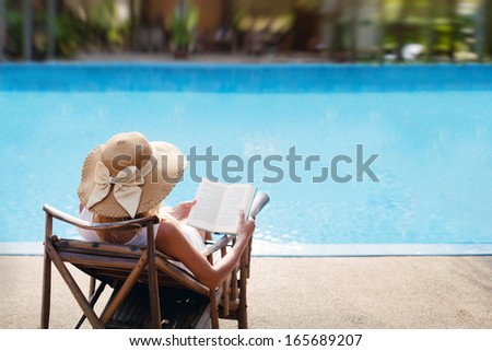 woman reading and relaxing near luxury swimming pool