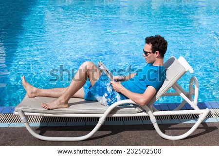 young man reading magazine near swimming pool in luxury hotel