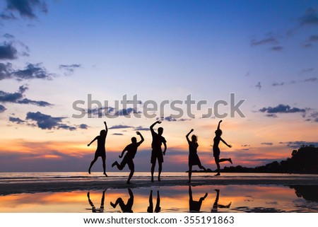 group of people jumping on the beach at sunset, silhouette of friends having fun together