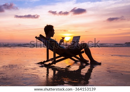 silhouette of successful business man reading emails on laptop on the beach at sunset, freelance job concept, work abroad