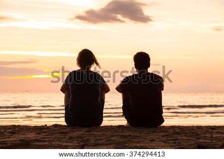 friends sitting together on the beach and watching sunset, friendship concept