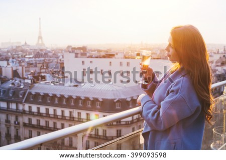 woman enjoying panoramic view of Paris and Eiffel tower at sunset, holding glass of wine or champagne in rooftop luxury restaurant