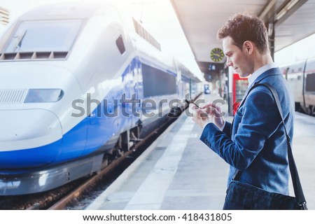 man using mobile application on his smartphone at train station, business travel