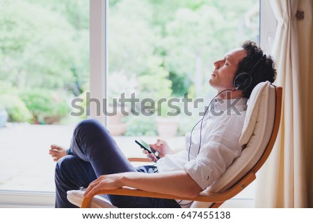 listening relaxing music at home, relaxed man in headphones sitting in deck chair in modern bright interior