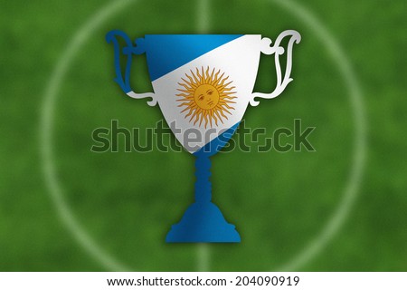 Soccer trophy with Argentina flag inside, field in the background.