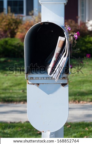 US Mail box with newspaper and letters in front of a house