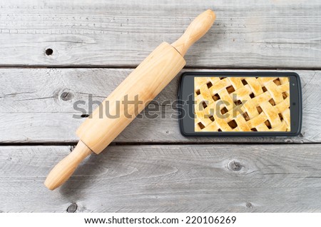 Rolling pin against old  wooden background and a mobile device showing details of apple pie crust