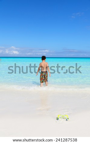 Back view of a little Asian boy heading towards blue tropical sea on a white sandy beach in Cayo Santa Maria, Cuba