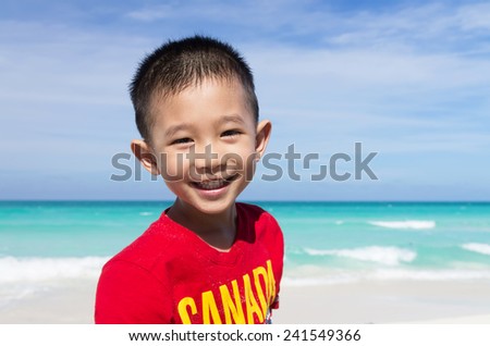 Cute little Asian boy standing on the beach all smiling wearing red Canada shirt