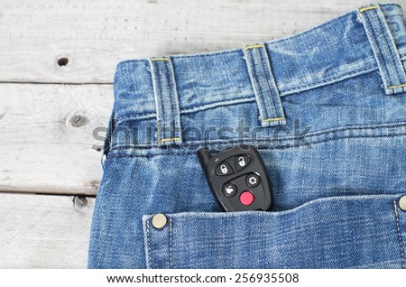 Car remote starter in blue jeans back pocket against wooden background