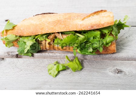 Banh Mi, Vietnamese sandwich filled with shredded chicken and coriander on a wooden table