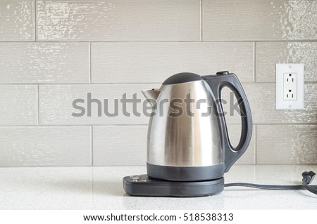 Electric stainless steel kettle on a granite counter top against a ceramic background