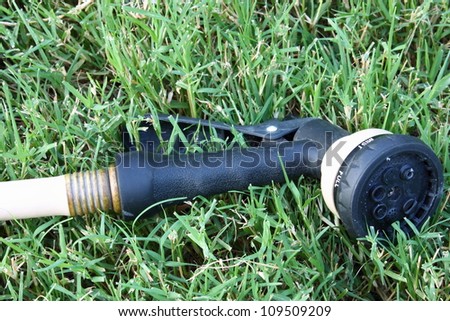 Water hose sprinkler laying in grass connected to a tan water hose.