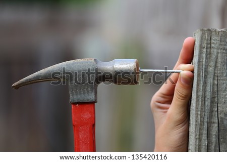 Close up view of a black and red hammer being used to hammer a nail into a fence post