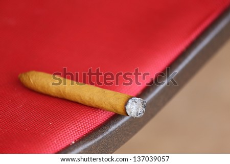 A close up view of a cigar burning laying on a chair