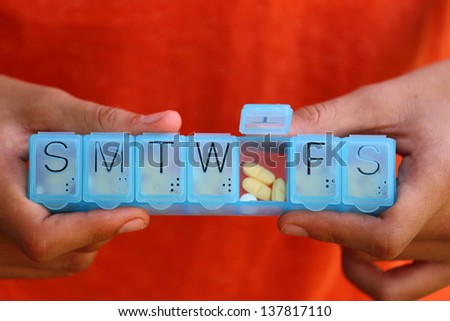 Close up view of someone holding a blue plastic 7 day pill box filled with pills