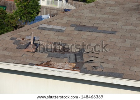 A close up view of shingles being blown off a roof and other roof damage