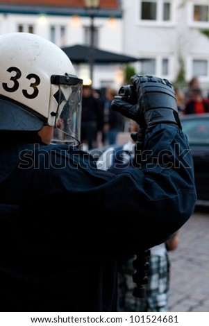 HAMBURG, GERMANY - MAY 1, 2012: Police officer in full riot gear films violent protesters during a May Day demonstration in Hamburg, Germany on May 1, 2012.