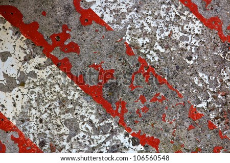 Detail of a pockmarked concrete wall painted in alternating bars of red and white at an industrial facility.