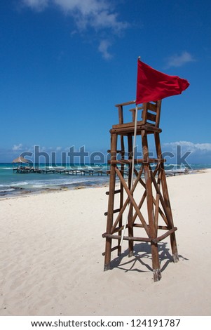 Empty lifeguard post with a red flag at a white, Caribbean beach under a clear sky.