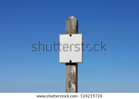 A white, empty sign on a weathered wooden signpost before a clear blue sky.