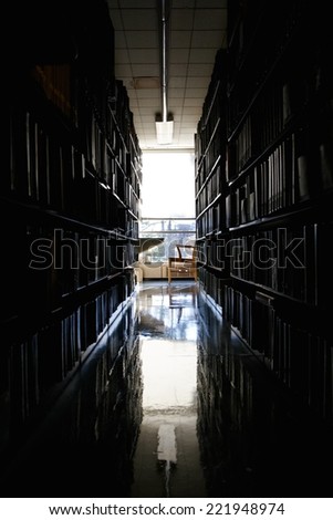 Quiet, secluded workplace at a university library, dark before stark bright light through a window.