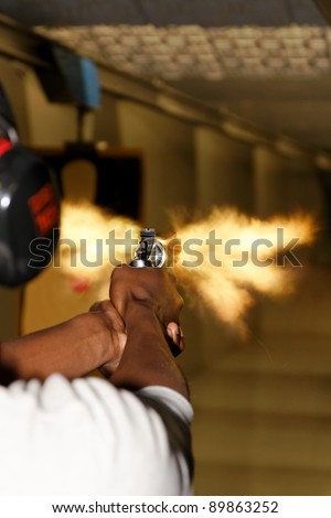 A picture taken over the shoulder of a young man firing a gun at a shooting range in the precise moment of the muzzle flash.