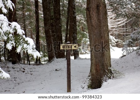 Sign on a wooden signpost in a snow-covered winter forest, pointing the reader toward an office.