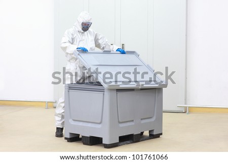 fully protected technician lifting cover of plastic container checking contents