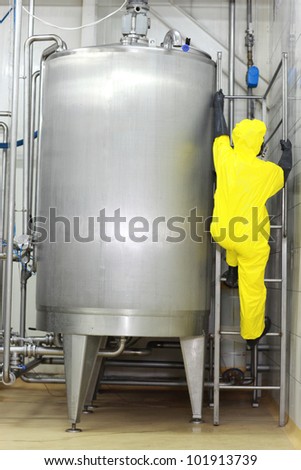 specialist in protective uniform going up a ladder on large industrial process tank in the factory
