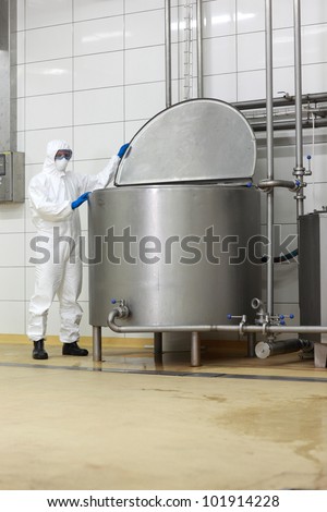technician in white protective uniform,mask,goggles,gloves  opening large industrial process tank in factory