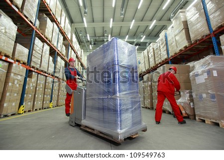 Warehousing -  Two workers in uniforms and safety helmets working in storehouse
