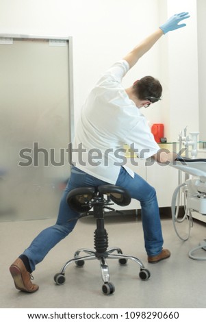 male dentist stretching his legs and arms in the office during break