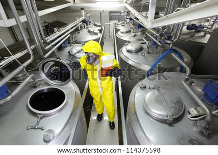 industrial professional with sample in container, in protective uniform,mask,goggle s,gloves and wellies controlling industrial process