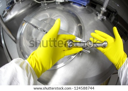 hands in yellow gloves closing industrial process tank