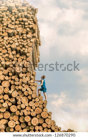 Challenge - Young man climbing the large pile of cut wooden logs