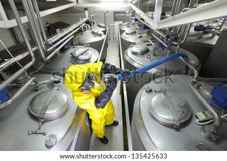 fully protected in yellow uniform,mask,and gloves technician  checking large process hose in factory