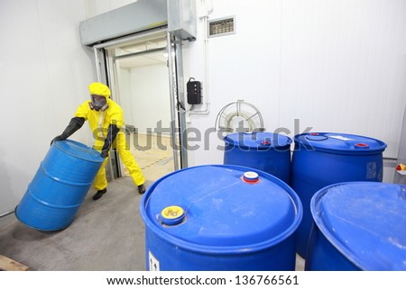 Worker in protective uniform,mask,gloves and boots rolling barrel of chemicals